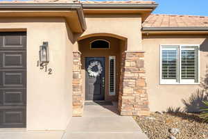 View of exterior entry with stucco siding, stone siding, and a tile roof