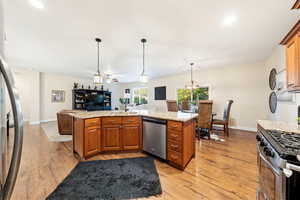 Kitchen with wood finish cabinets, light stone counters, stainless steel appliances, light wood-style flooring, and open floor plan
