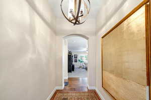 Hallway with arched walkways, dark wood-type flooring, and suspended lighting