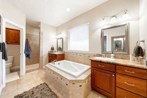 Full bath with two vanities, a walk in shower, a whirlpool tub, light tile patterned floors, and recessed lighting