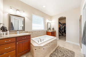 Bathroom with a walk in closet, two vanities, light tile patterned floors, a bath, and recessed lighting