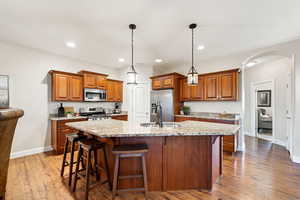 Kitchen with wood finish cabinetry, arched walkways, a center island with sink, a breakfast bar, and dark wood finished floors