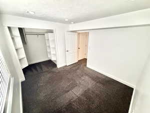 Unfurnished bedroom with dark colored carpet, a closet, and a textured ceiling