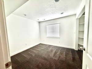 Empty room with dark carpet and a textured ceiling