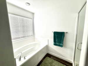 Full bath featuring a garden tub, a shower stall, dark wood-type flooring, and a textured ceiling