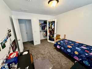 Bedroom featuring dark colored carpet, a walk in closet, and a textured ceiling