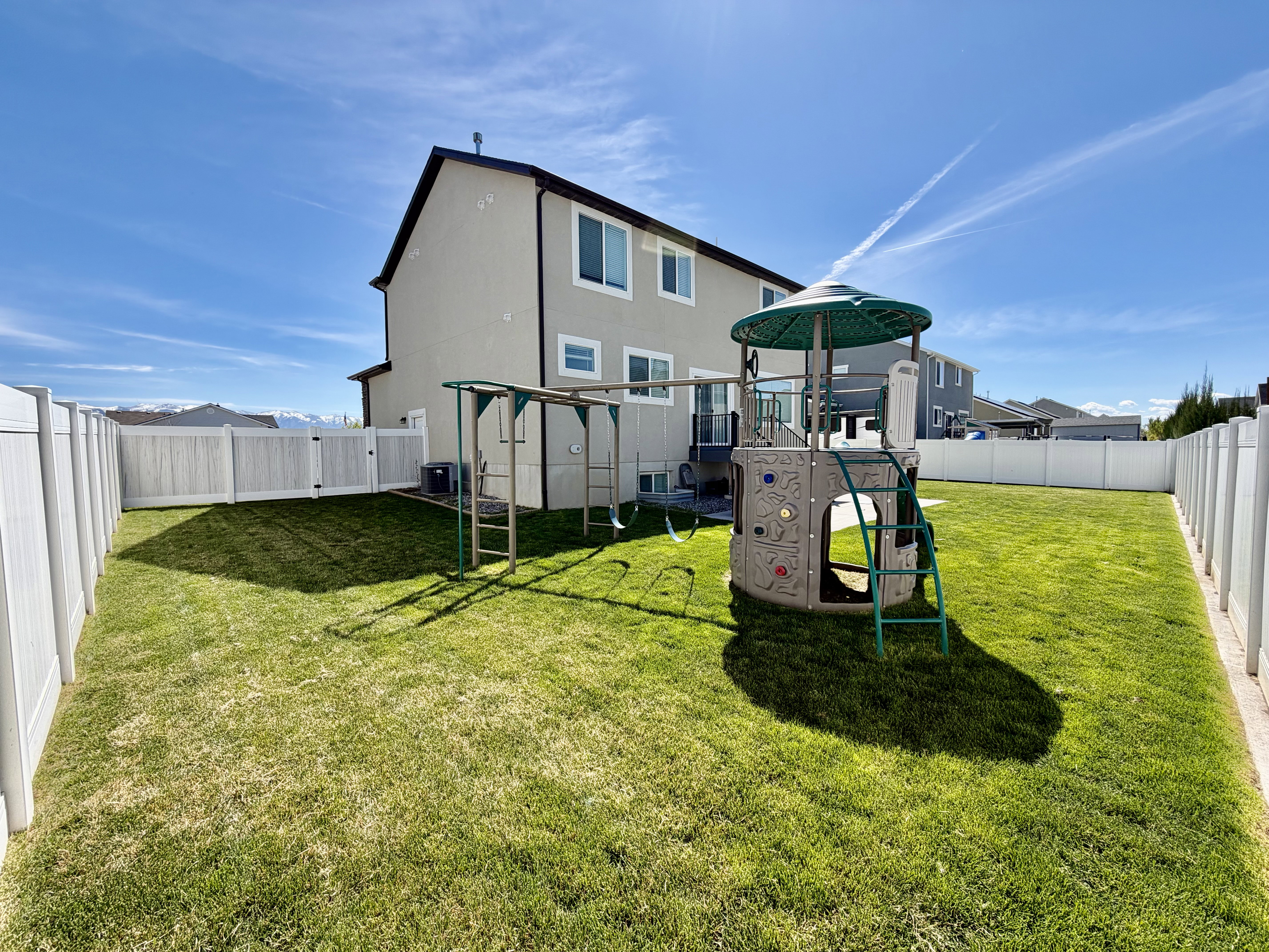 Back of property with a fenced backyard, a playground, and stucco siding