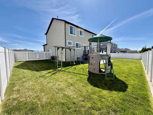 Back of property with a fenced backyard, a playground, and stucco siding
