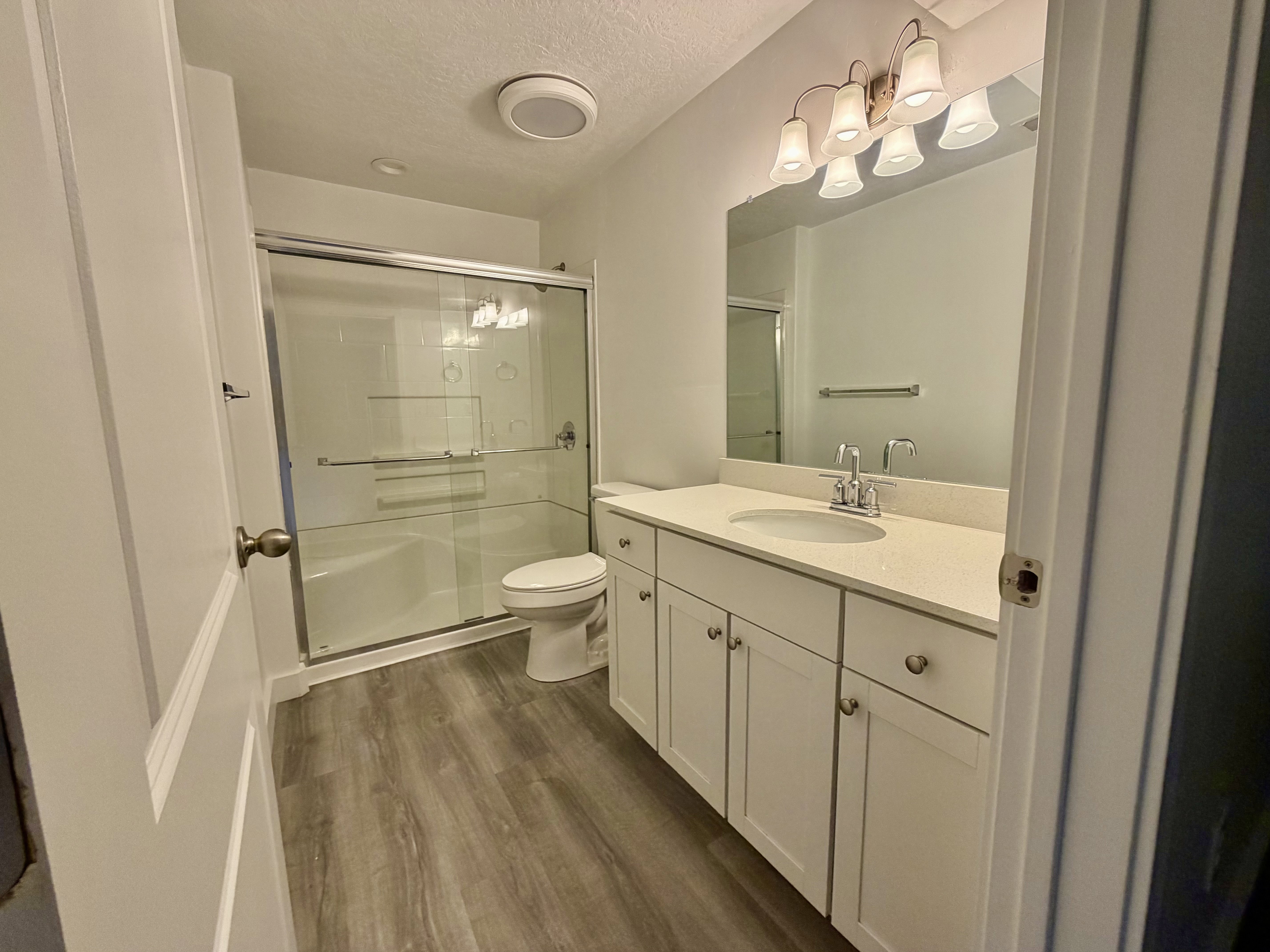 Bathroom featuring a textured ceiling, vanity, dark wood-style flooring, a stall shower, and hanging lights