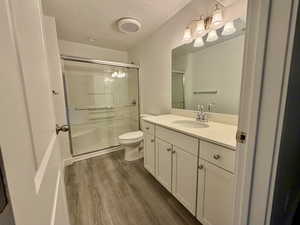 Bathroom featuring a textured ceiling, vanity, dark wood-style flooring, a stall shower, and hanging lights