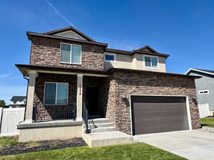 View of front facade with covered porch, stone siding, concrete driveway, and stucco siding