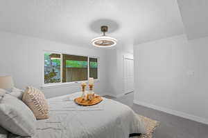 Bedroom with a closet, dark carpet, a textured ceiling, and a ceiling fan