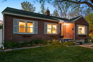 View of front of property featuring a front lawn, brick siding, a chimney, and roof with shingles