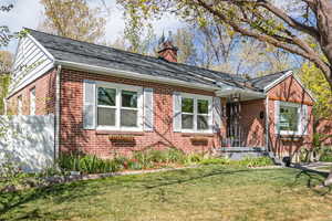 View of front of home featuring a porch, a front yard, brick siding, a chimney, and roof with shingles