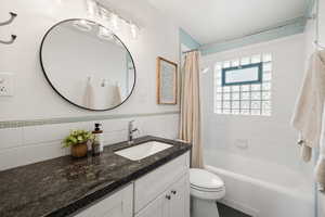 Full bathroom featuring shower / bathtub combination with curtain, tile walls, vanity, and wainscoting