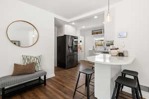 Kitchen featuring a breakfast bar area, stainless steel fridge, decorative light fixtures, white cabinetry, and dark wood-style floors