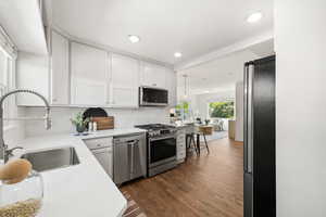 Kitchen with stainless steel appliances, white cabinets, dark wood finished floors, hanging light fixtures, and light stone counters