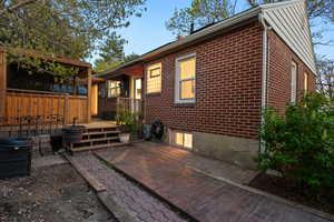 Rear view of property featuring brick siding, a wooden deck, and a patio