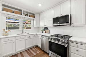 Kitchen with white cabinetry, stainless steel appliances, dark wood finished floors, light stone counters, and recessed lighting