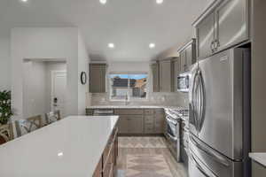Kitchen featuring stainless steel appliances, a kitchen breakfast bar, light stone counters, gray cabinetry, and recessed lighting