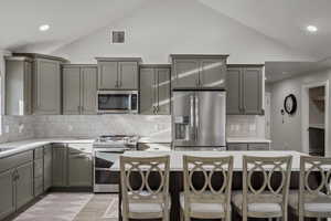 Kitchen featuring gray cabinets, recessed lighting, stainless steel appliances, decorative backsplash, and a breakfast bar
