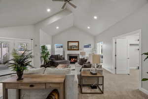 Living room featuring a warm lit fireplace, a ceiling fan, light carpet, vaulted ceiling, and recessed lighting