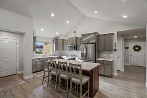 Kitchen featuring a kitchen breakfast bar, a center island, stainless steel appliances, light wood-style flooring, and lofted ceiling