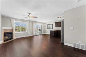 Unfurnished living room featuring dark wood-style flooring, a fireplace, ceiling fan, and plenty of natural light