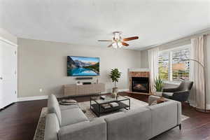 Living room with dark wood-type flooring, a tile fireplace, and a ceiling fan