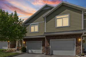 View of front of home featuring stone siding, a garage, driveway, and roof with shingles