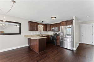 Kitchen with stainless steel appliances, a chandelier, a peninsula, and dark wood finish cabinets