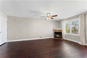Unfurnished living room featuring dark wood-style flooring, a fireplace, a ceiling fan, and a textured ceiling