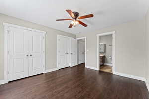 Unfurnished bedroom featuring multiple closets, dark wood-type flooring, a ceiling fan, and connected bathroom