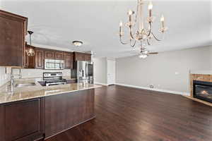 Kitchen featuring dark wood finish cabinets, stainless steel appliances, light stone counters, a tiled fireplace, and dark wood-type flooring