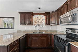 Kitchen with stainless steel appliances, dark wood finish cabinetry, a peninsula, and light stone counters