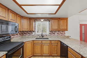 Kitchen with black appliances, wood finish cabinetry, and light stone counters