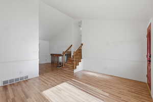 Unfurnished living room featuring light wood-style floors and vaulted ceiling