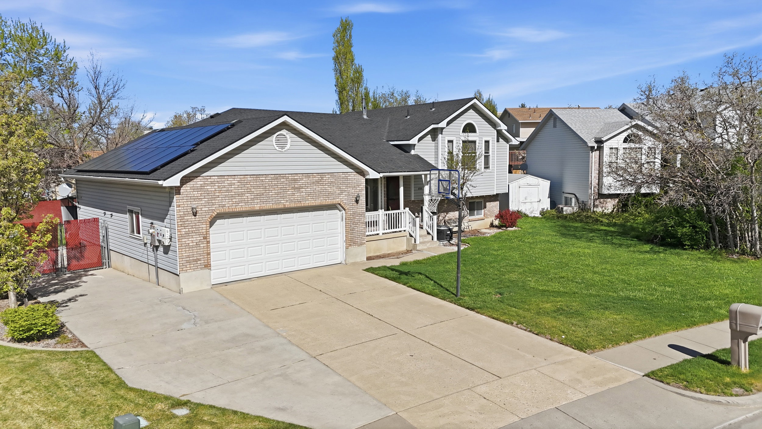 Tri-level home featuring concrete driveway, brick siding, a front lawn, roof mounted solar panels, and a garage