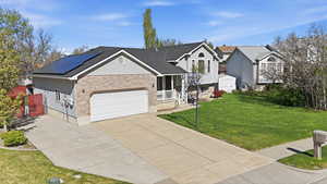Tri-level home featuring concrete driveway, brick siding, a front lawn, roof mounted solar panels, and a garage