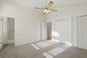 Unfurnished bedroom featuring light colored carpet, multiple closets, connected bathroom, a ceiling fan, and lofted ceiling