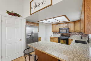 Kitchen with black appliances, a peninsula, backsplash, light wood-style flooring, and wood finish cabinetry