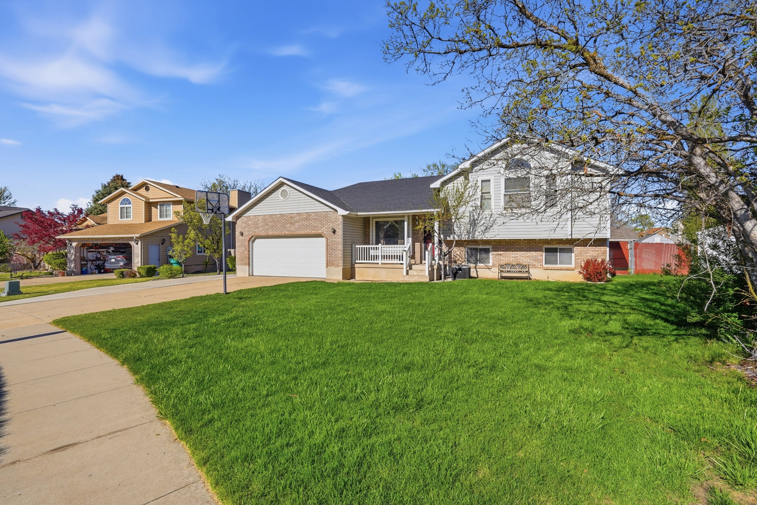Split level home with covered porch, concrete driveway, brick siding, and an attached garage