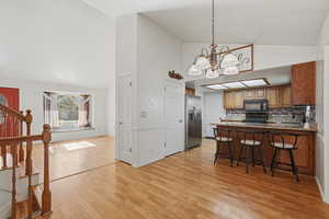 Kitchen featuring lofted ceiling, suspended lighting, a breakfast bar, a peninsula, and wood finish cabinetry