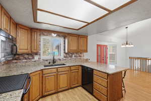 Kitchen with wood finish cabinetry, a peninsula, light stone counters, and vaulted ceiling