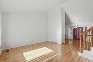 Spare room featuring vaulted ceiling, light wood-type flooring, and hanging lights