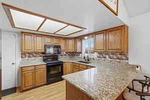 Kitchen with wood finish cabinets, a peninsula, black appliances, and light stone countertops