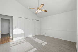 Unfurnished bedroom with two closets, light carpet, vaulted ceiling, and ceiling fan