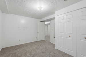 Unfurnished bedroom with a textured ceiling, light colored carpet, and a closet