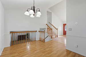Unfurnished room with light wood-style floors, suspended lighting, a fireplace, and vaulted ceiling