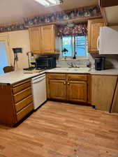 Kitchen with white appliances, light countertops, a peninsula, wood finish cabinetry, and light wood-type flooring